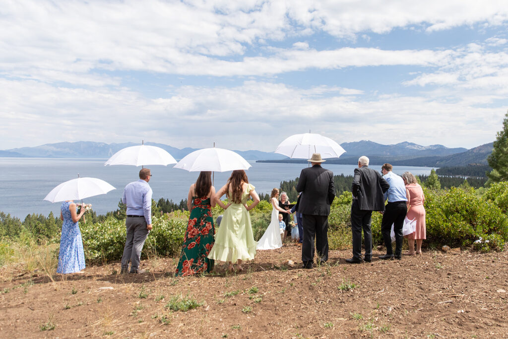 a micro wedding ceremony in lake tahoe, guests holding white umbrellas to shield themselves from the weather