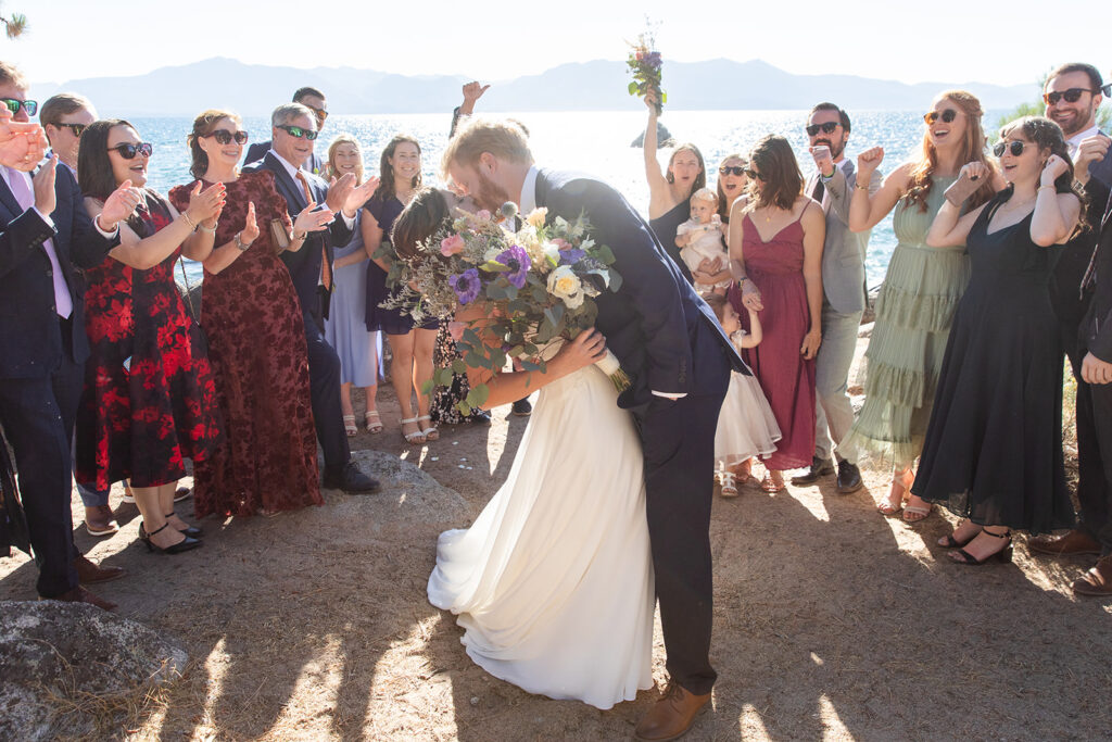 bride and groom first kiss surrounded by their loved ones