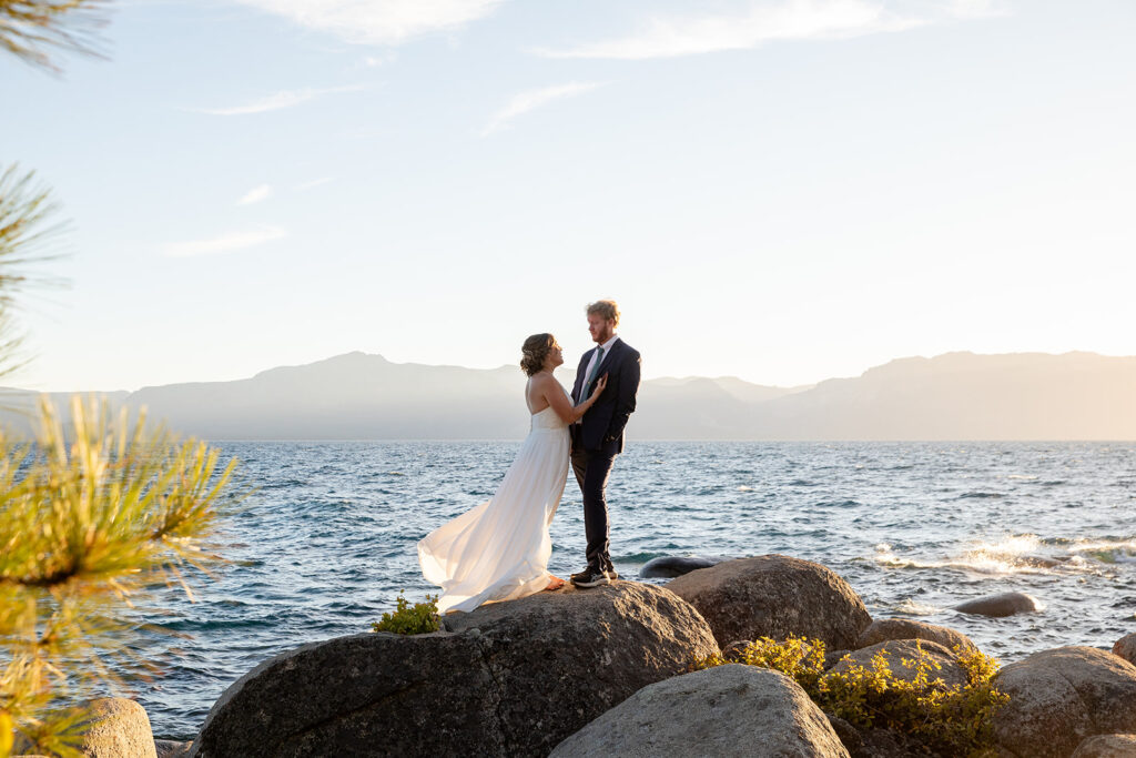 bride and groom hugging on a large rock surrounded by water views