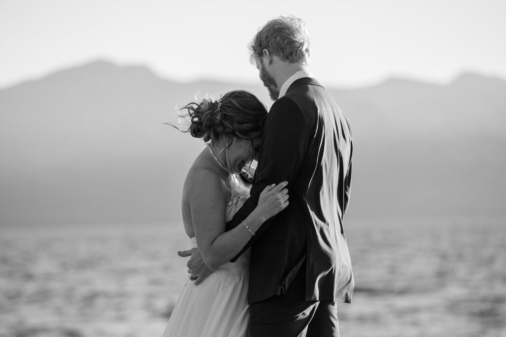 bride and groom hugging on a large rock surrounded by water views