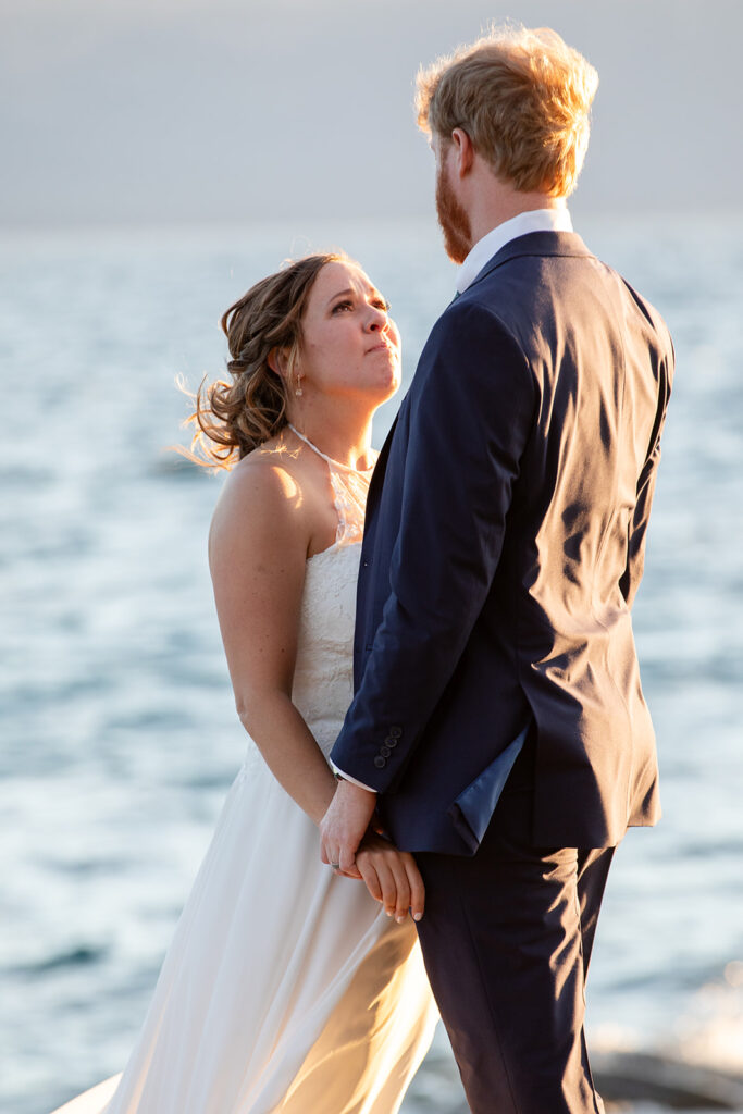 bride and groom hugging on a large rock surrounded by water views