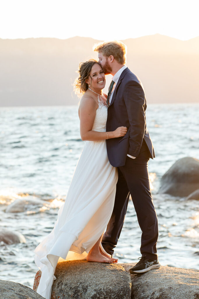 bride and groom hugging on a large rock surrounded by water views