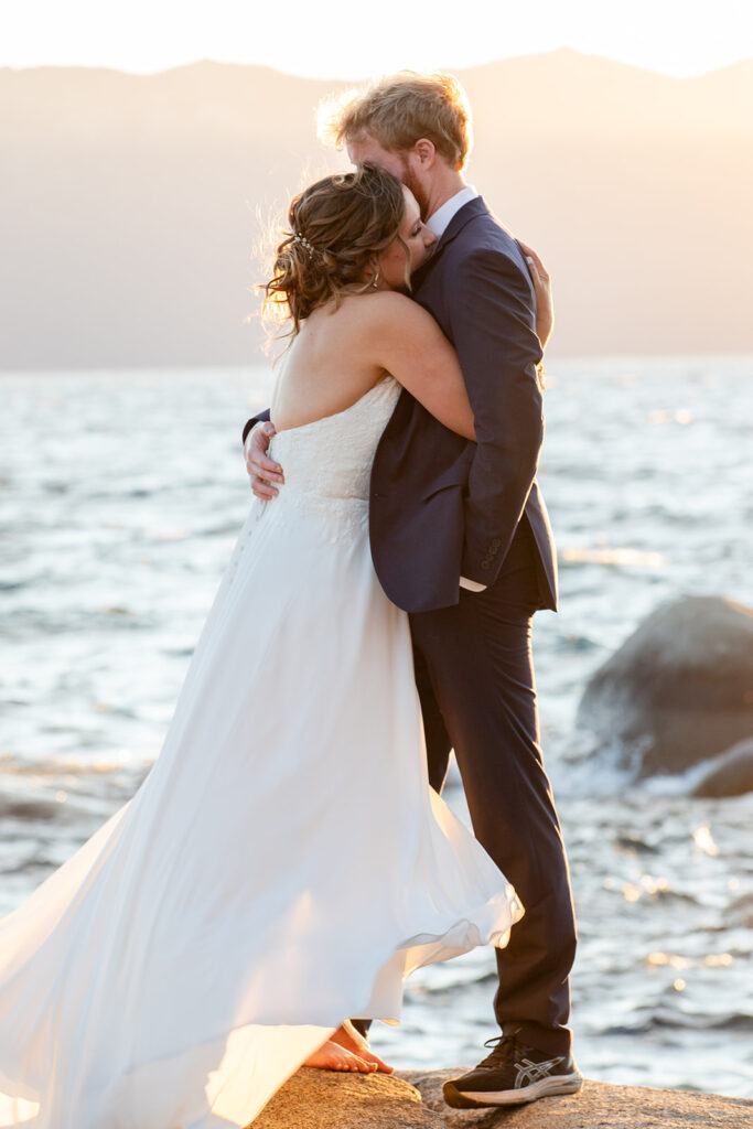 bride and groom hugging on a large rock surrounded by water views